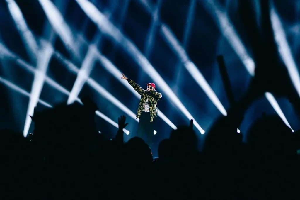 Performer on stage during a live concert with dramatic lighting and audience silhouettes in the foreground