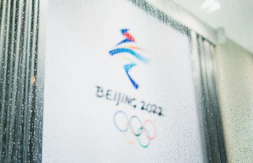Beijing 2022 Winter Olympics logo viewed through a glass window, symbolizing China’s growing national focus on sports and athletic culture.