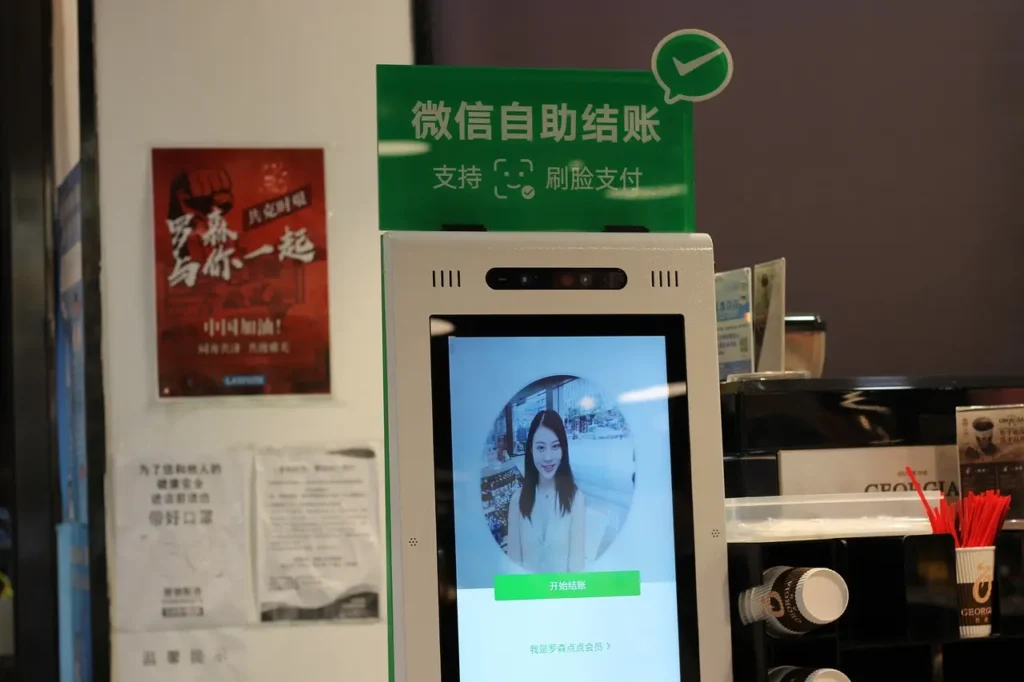 WeChat self-service checkout terminal in a store, displaying a facial recognition payment screen with a customer’s face on the monitor.