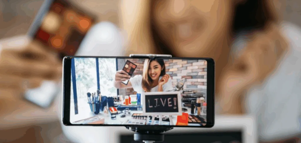 Influencer hosting a live commerce beauty stream using a smartphone setup with makeup products displayed on a table
