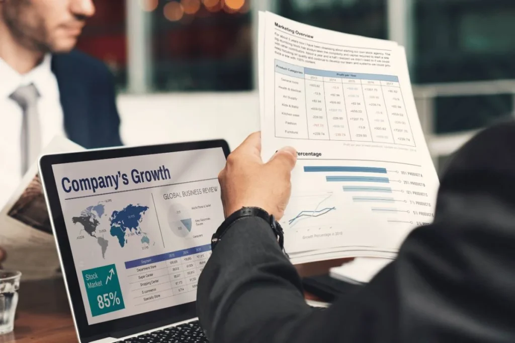 Business professionals reviewing printed financial reports alongside a laptop displaying company growth data