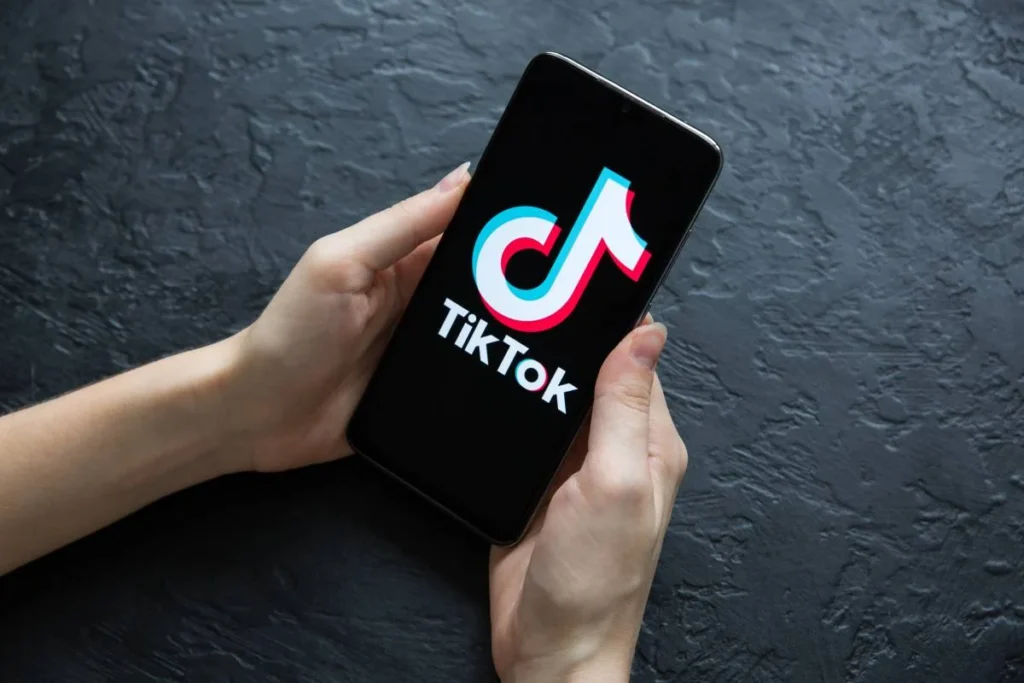 Smartphone held in both hands displaying the TikTok app logo on a dark background