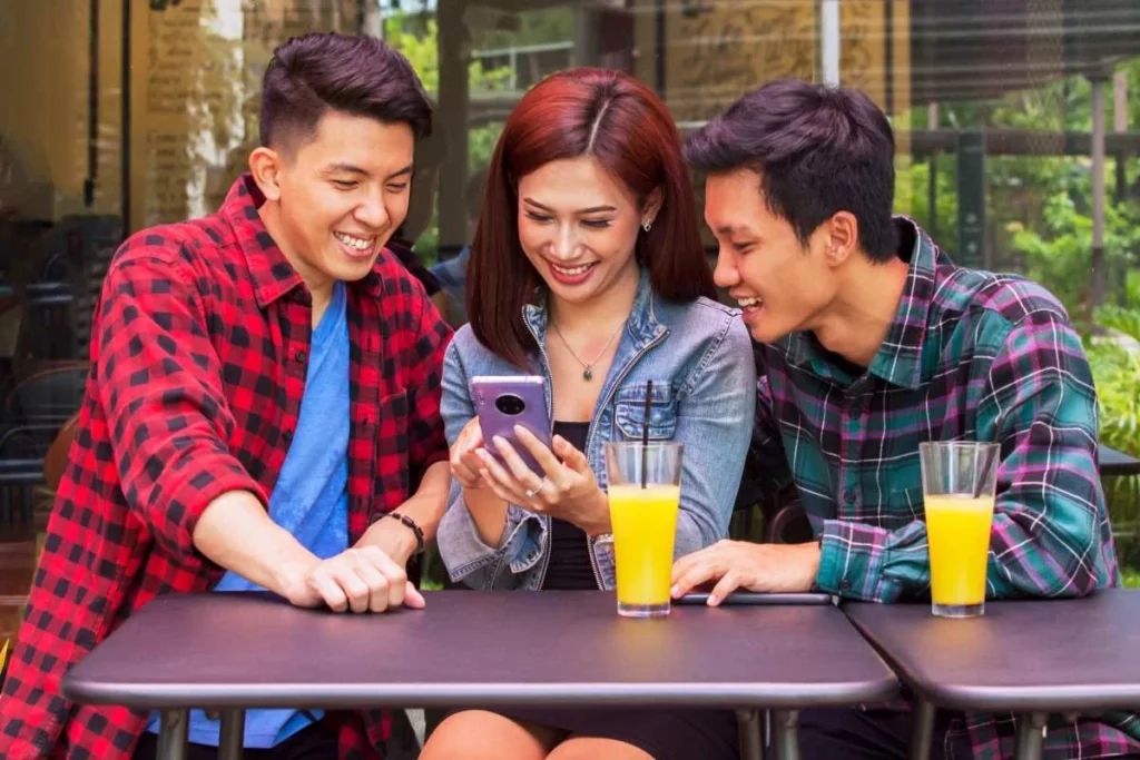Three young adults sitting at a café table watching a short video together on a smartphone