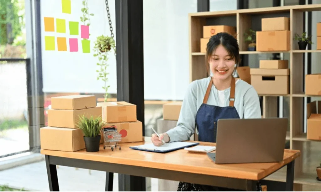 Woman packing boxes and working on a laptop in a small business workspace