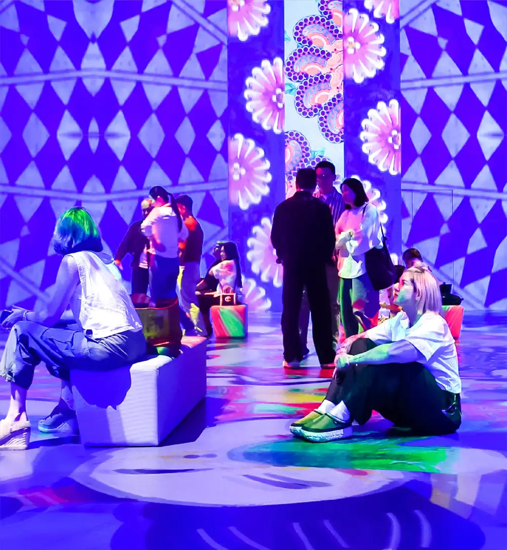 Visitors relaxing inside immersive digital art installation with colorful projections