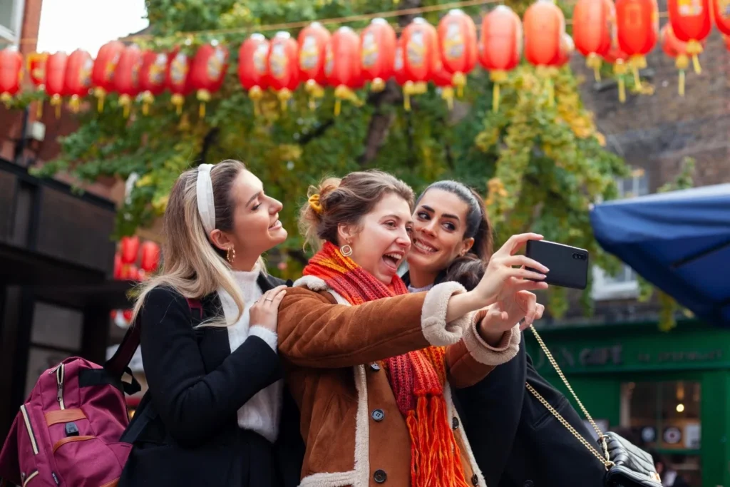 Three friends taking a selfie under red lanterns during the Chinese Lantern Festival, enjoying the colorful decorations and capturing the moment together.